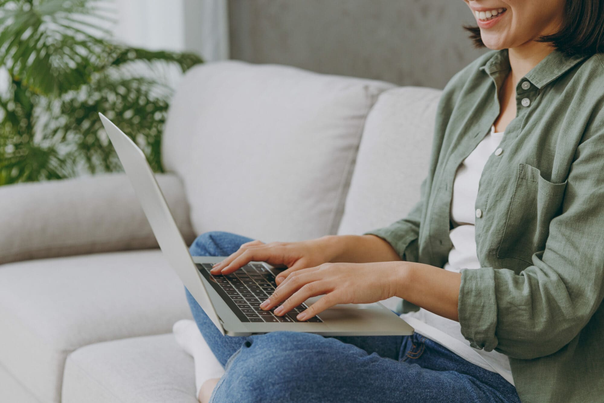 Cropped close up fun young fun IT woman wears casual clothes hold use work on laptop pc computer sits on grey sofa couch stay at home hotel flat rest relax spend free spare time in living room indoor.
